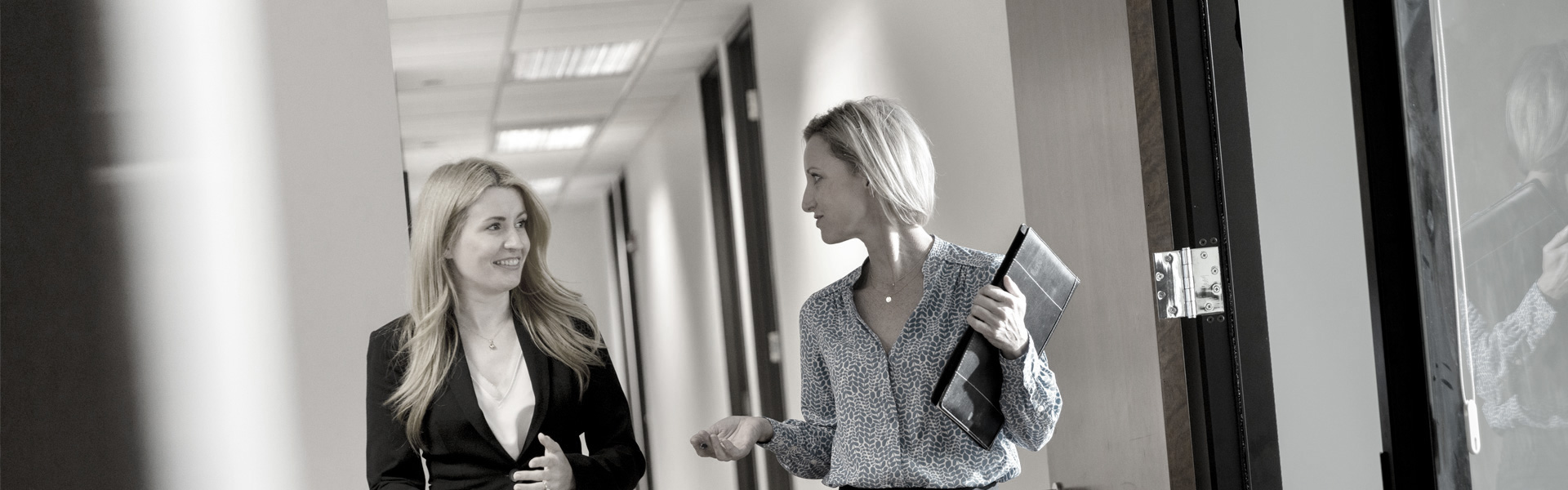 two women walking down an office hallway while talking